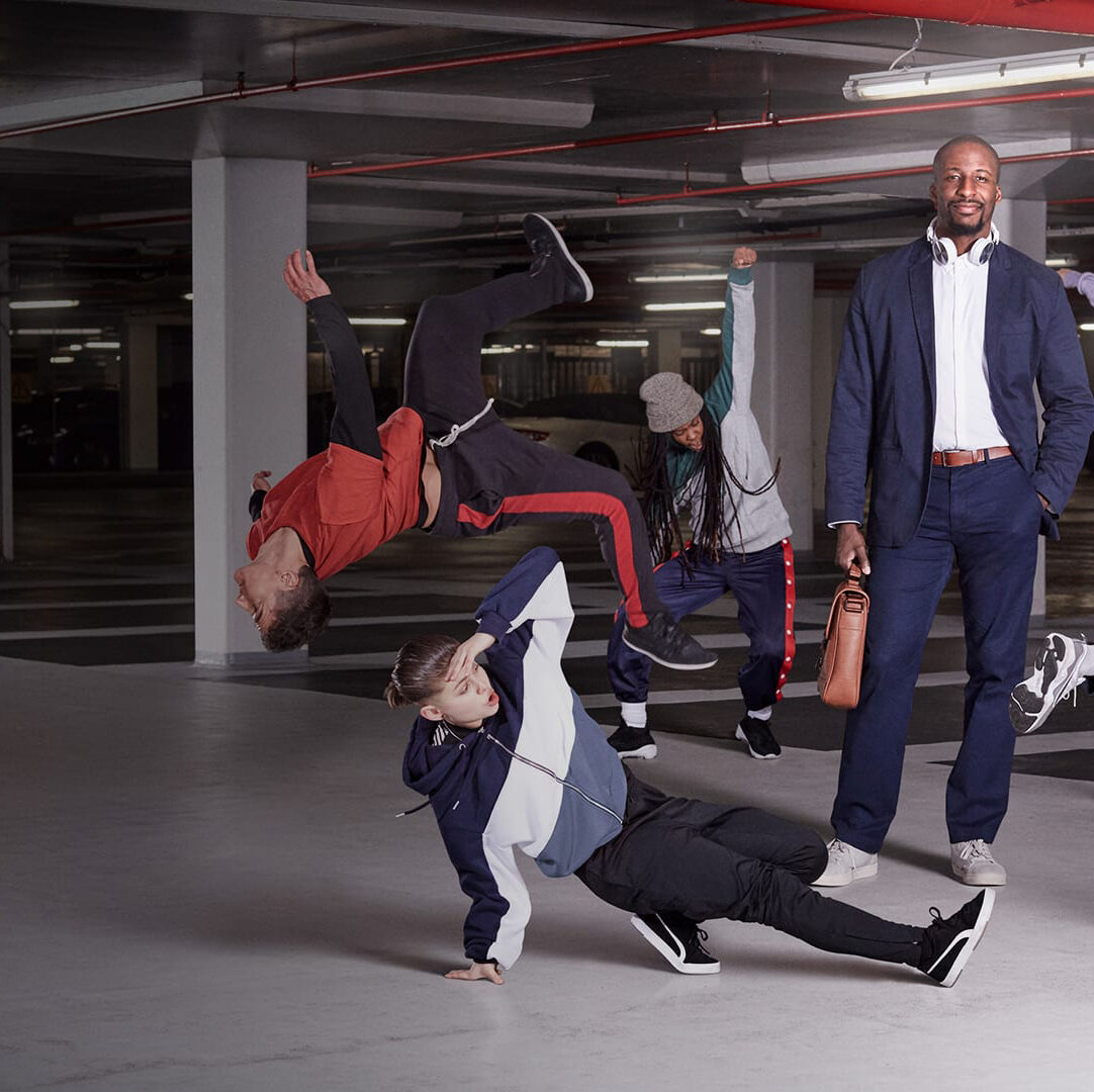 Business professional walking confidently while breakdancers perform dynamic moves in underground parking garage