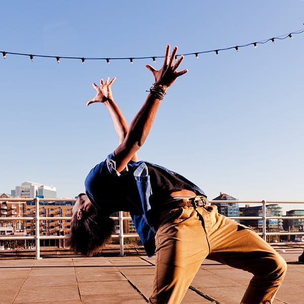 A person dances energetically against a clear sky with city buildings in the background.