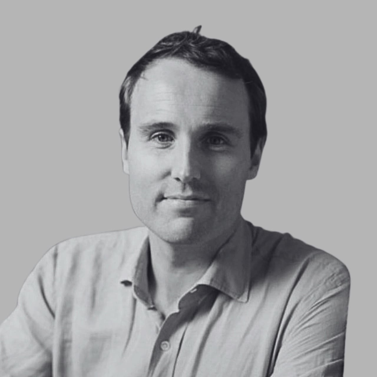 A man with short hair smiles at the camera, wearing a light-colored shirt against a gray background.