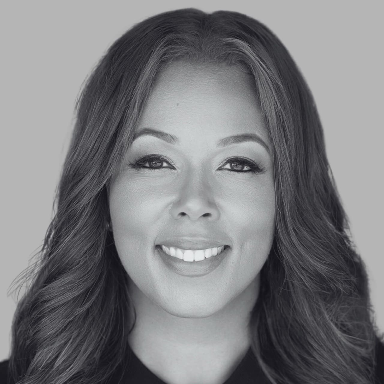 Black and white portrait of a smiling woman with long, wavy hair against a gray background.