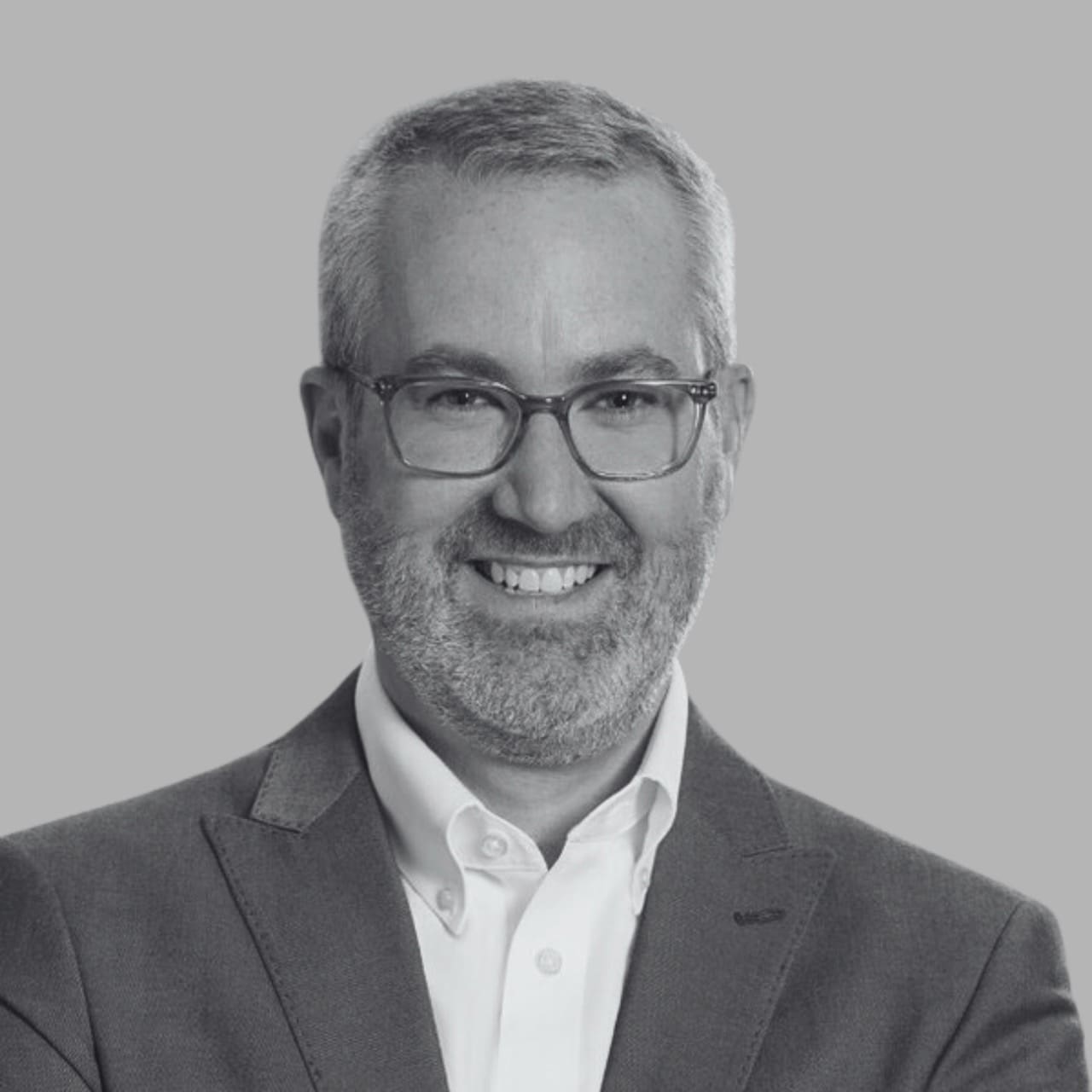 Smiling individual in a suit with glasses against a gray background.