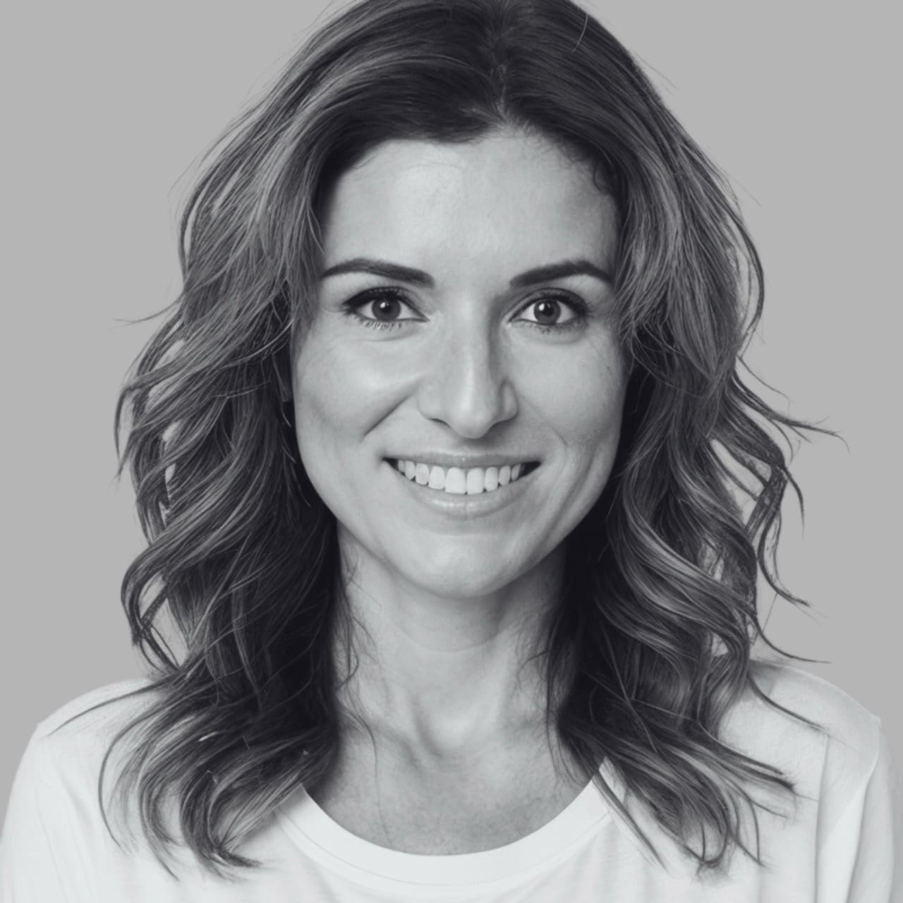 Smiling woman with wavy hair wearing a white shirt, against a gray background.