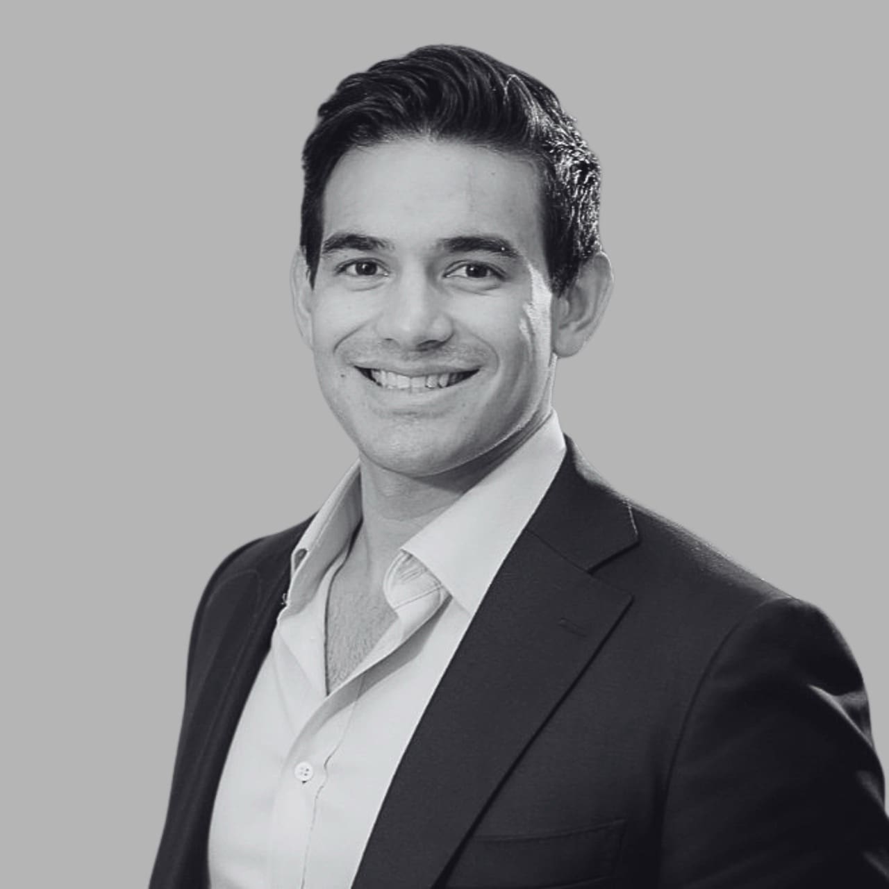 Smiling man in a suit with a white shirt, set against a grey background.