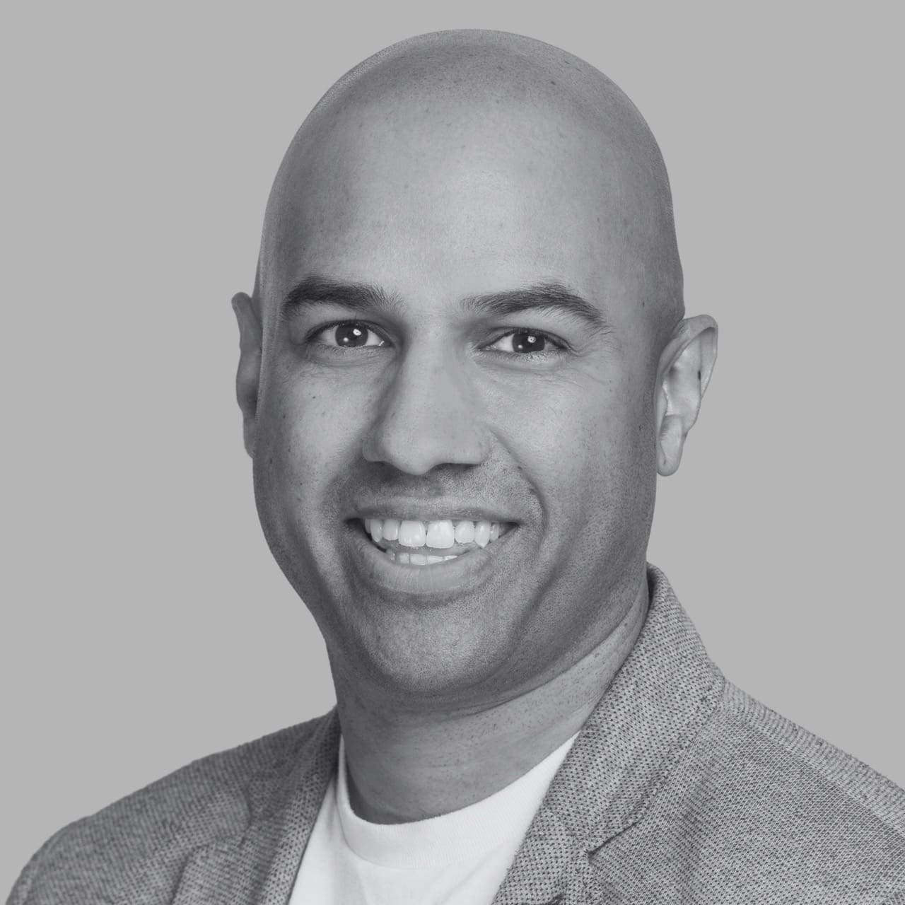 Professional headshot of a smiling bald man in a textured blazer and white shirt