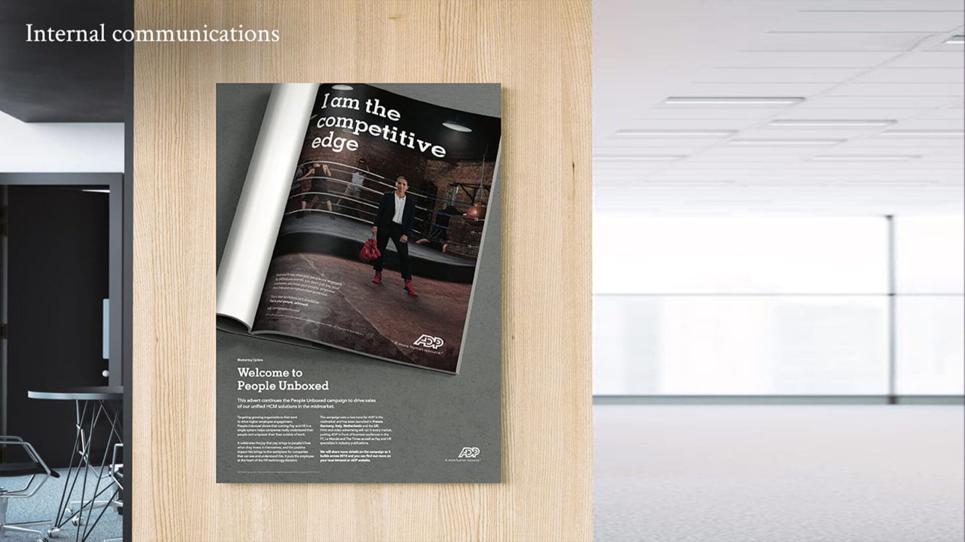 A poster displayed on a wooden wall features an image of a person in a boxing ring, wearing a suit and holding red boxing gloves. The text reads, "I am the competitive edge" at the top, while the bottom says, "Welcome to