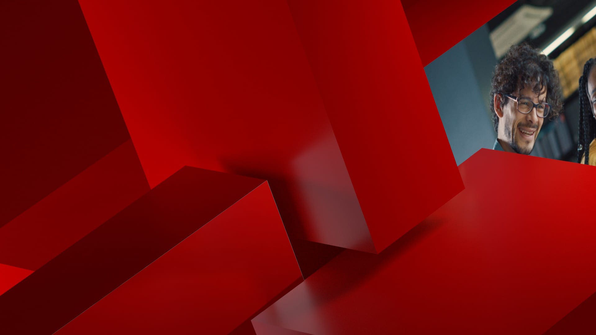 Two people smiling amidst a background of red geometric shapes.