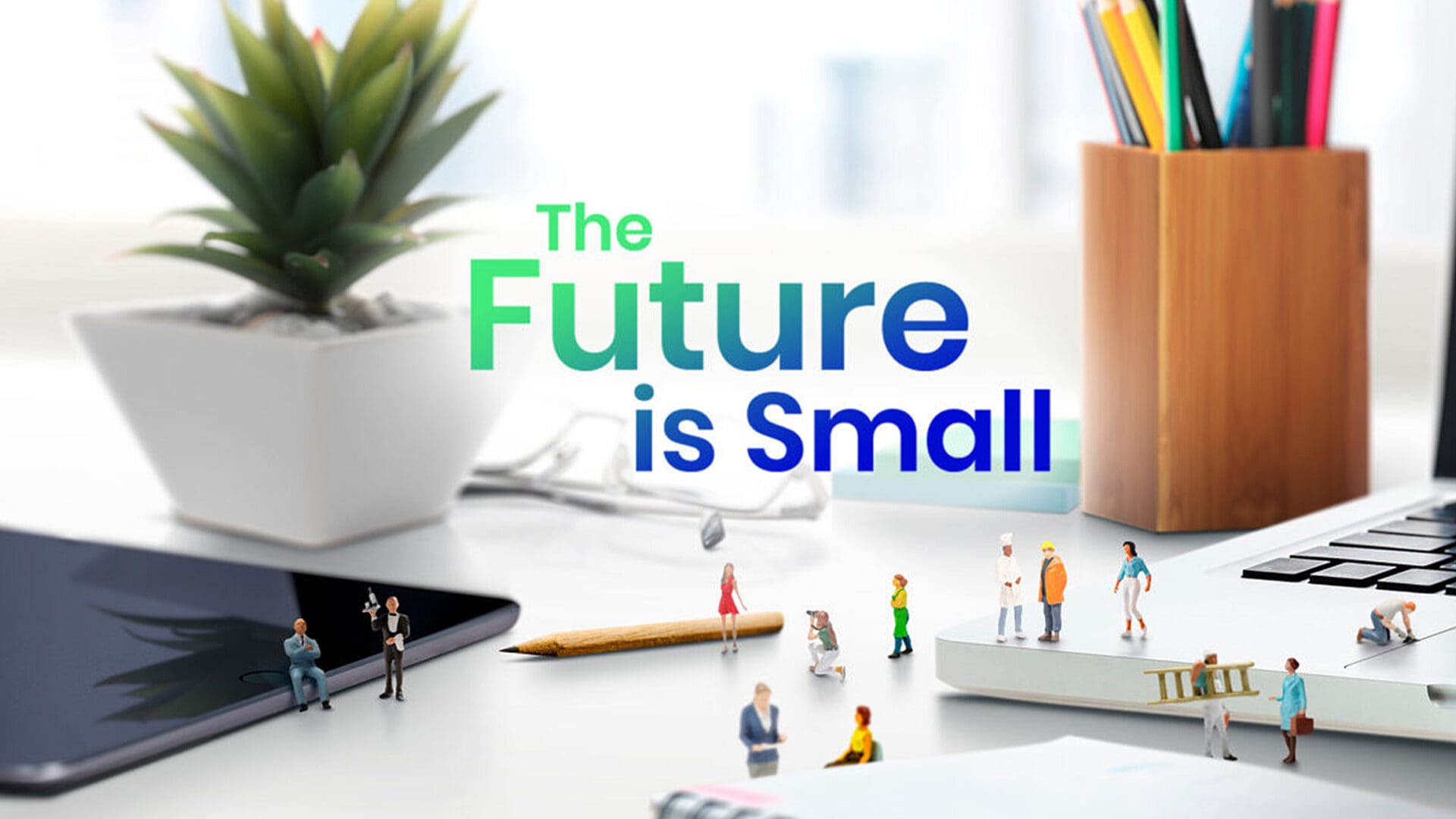 "Miniature figures on a desk with text: 'The Future is Small,' alongside a plant and tools."